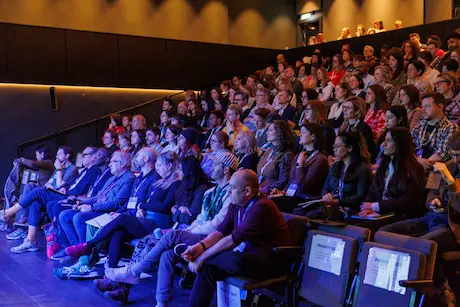 Rows of attendees in tiered seats listening to a talk.