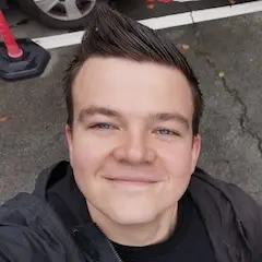 A smiling young man with short hair taking a selfie from above outdoors.