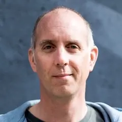 A man with short hair wearing a hoodie and a little bit of a smile.